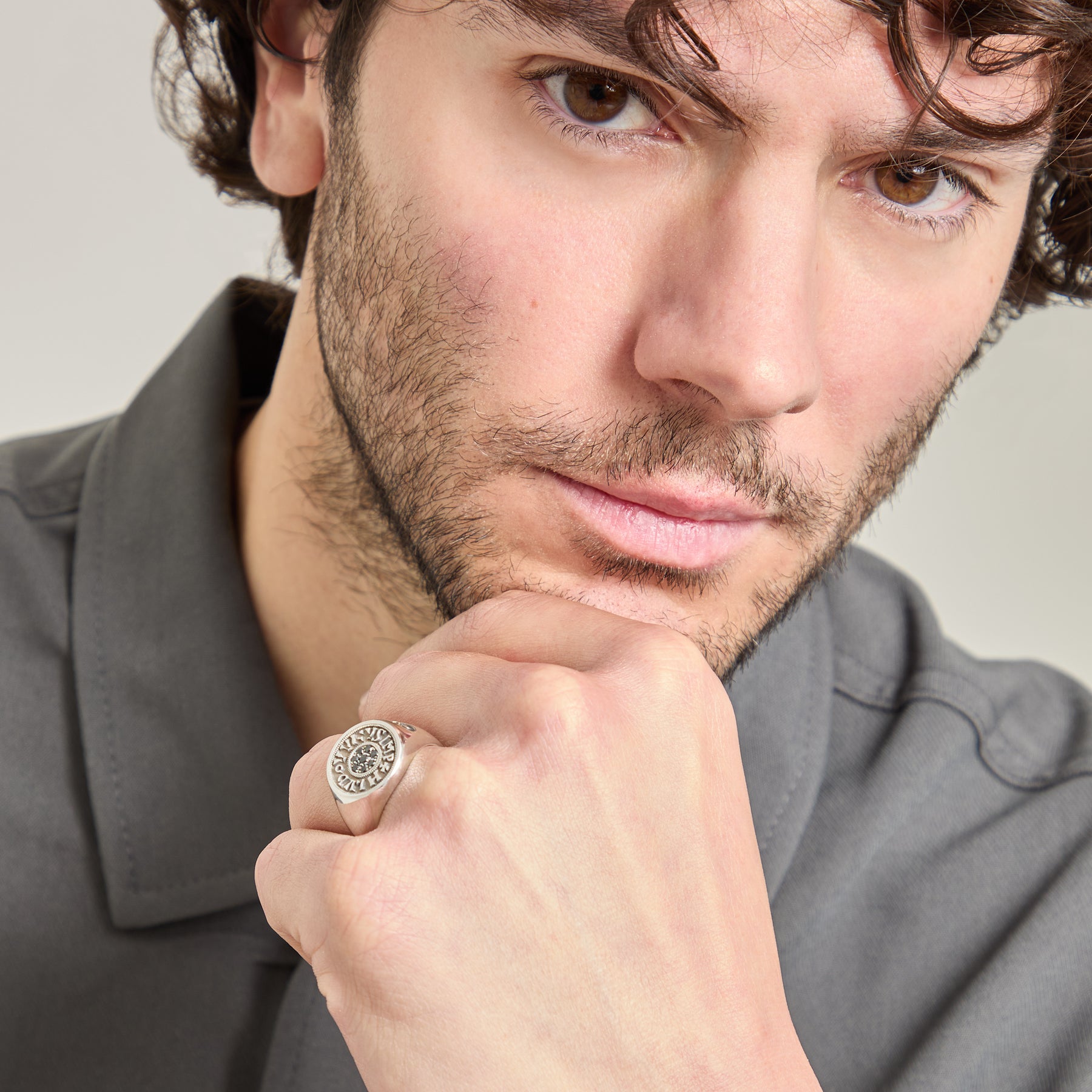 Man wearing a ring with a gray shirt on a neutral background