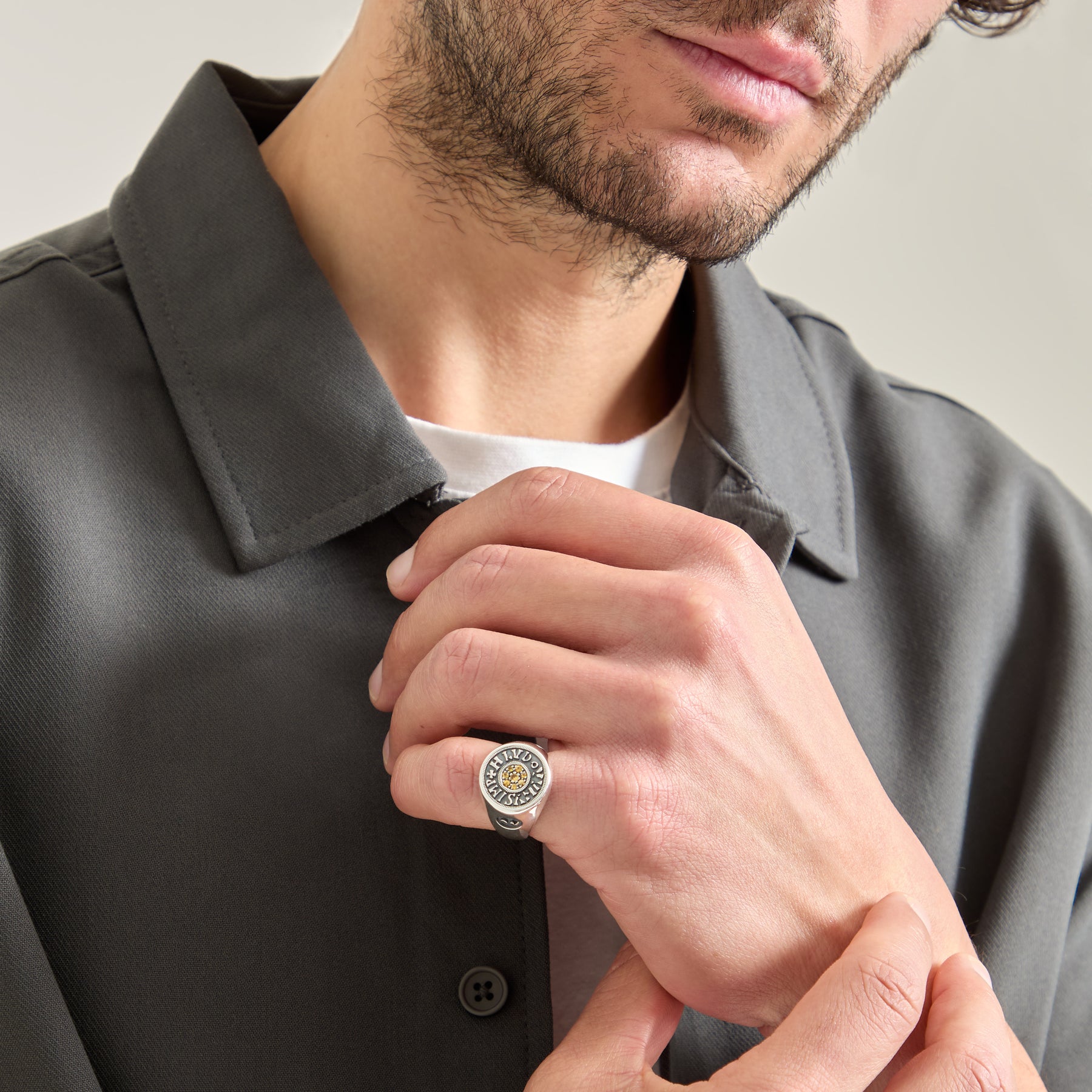 Man wearing a gray shirt with a decorative ring on his finger against a neutral background