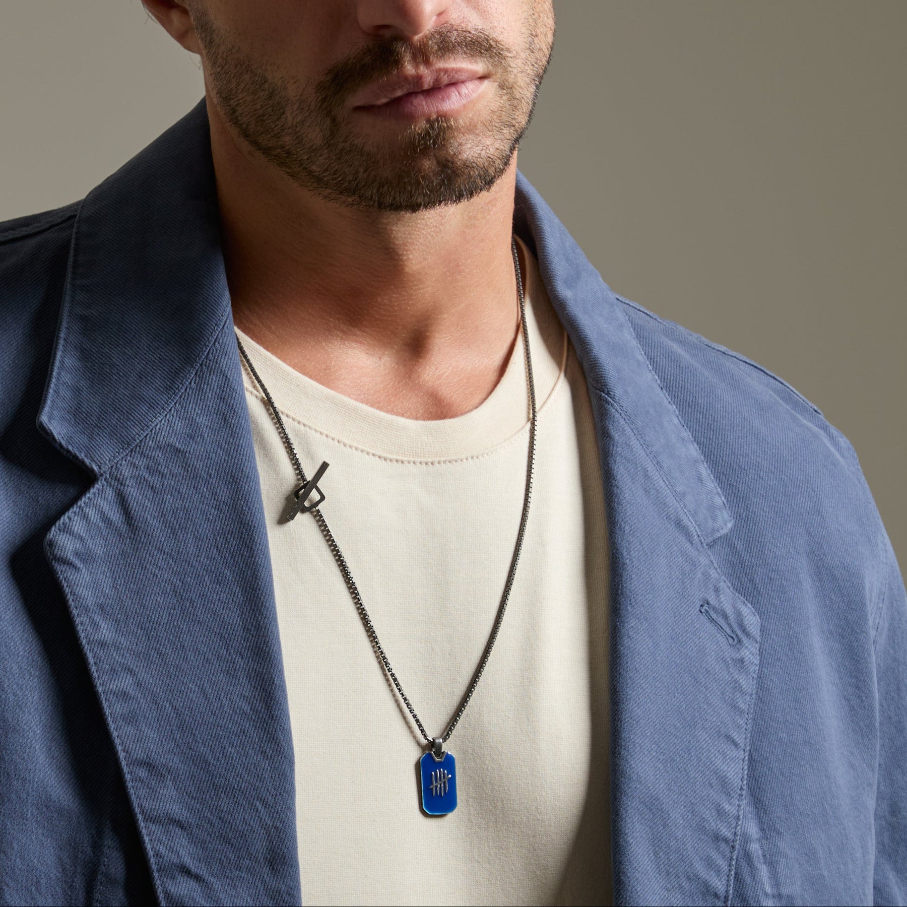 Man wearing a blue coat and white shirt with a necklace on a gray background