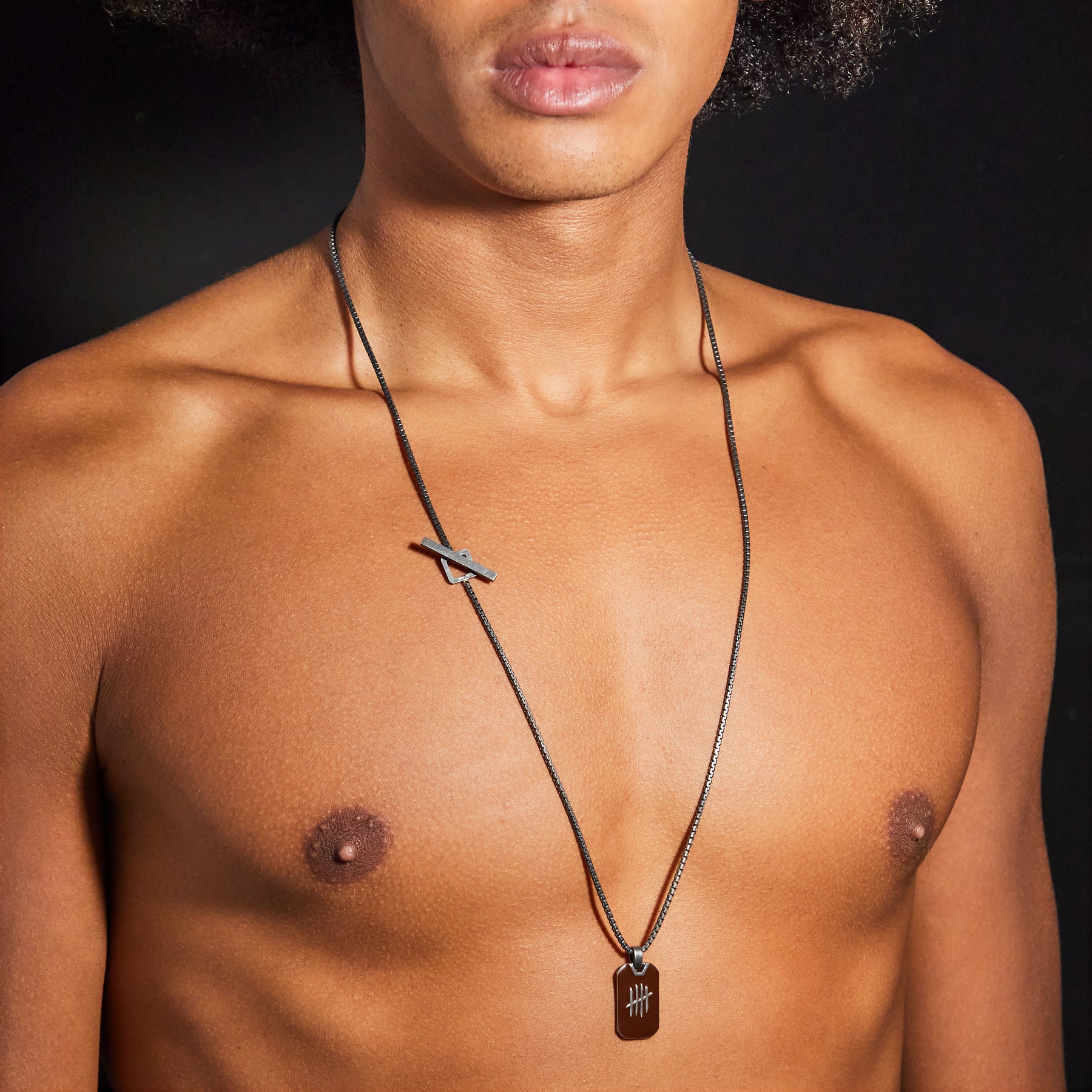 Man wearing a necklace with a pendant on a dark background