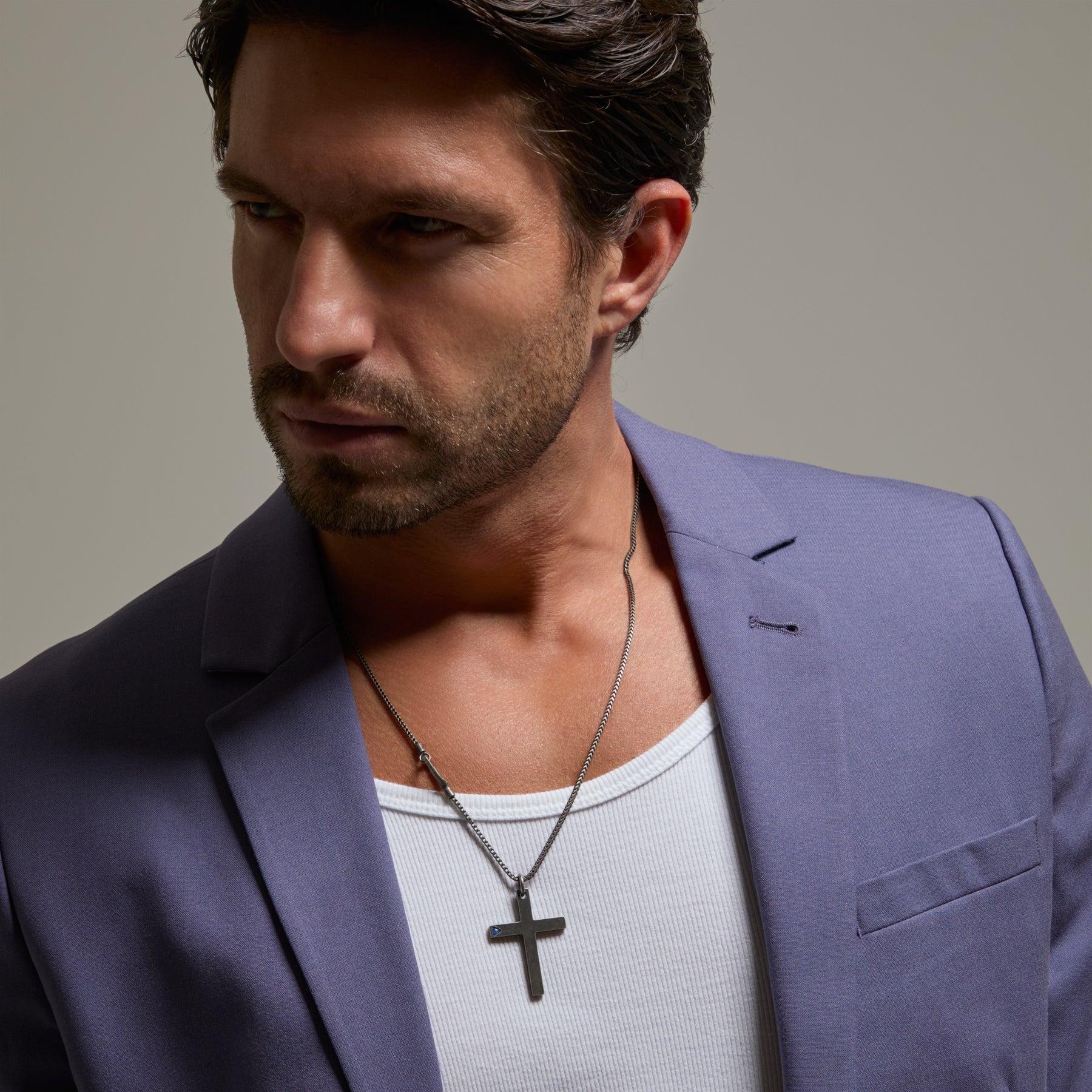 Man wearing a purple blazer over a white shirt with a necklace featuring a cross pendant.