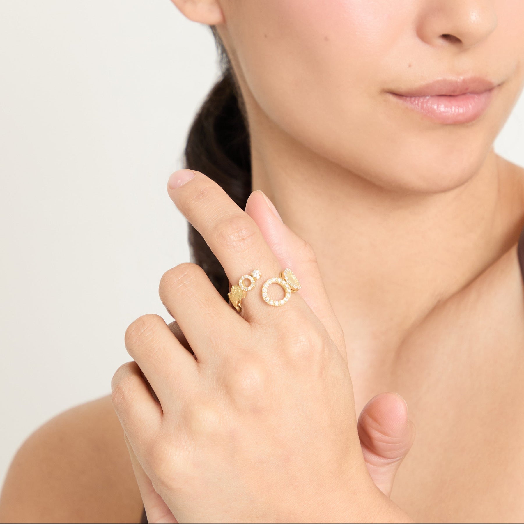 Woman wearing a gold ring on her finger against a plain background