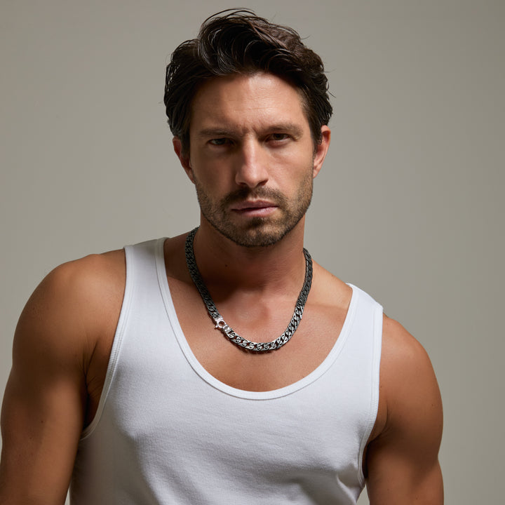 Man wearing a white tank top and chain necklace against a neutral background