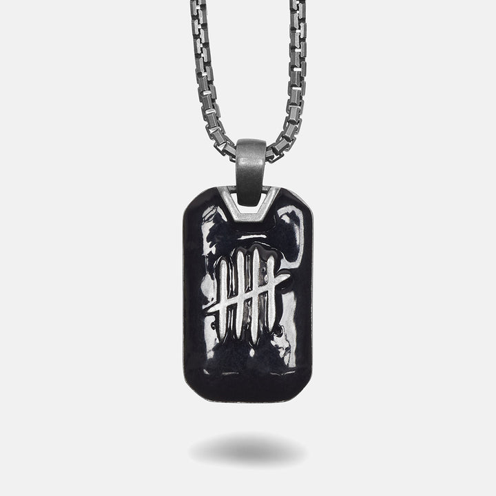 Black dog tag pendant on a chain against a white background