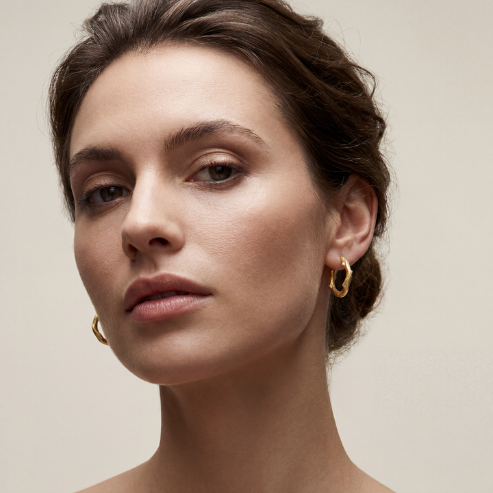 Close-up of a woman wearing gold earrings against a beige background