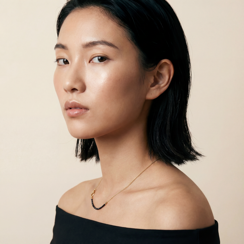 Woman with short black hair wearing a black off-shoulder top against a beige background