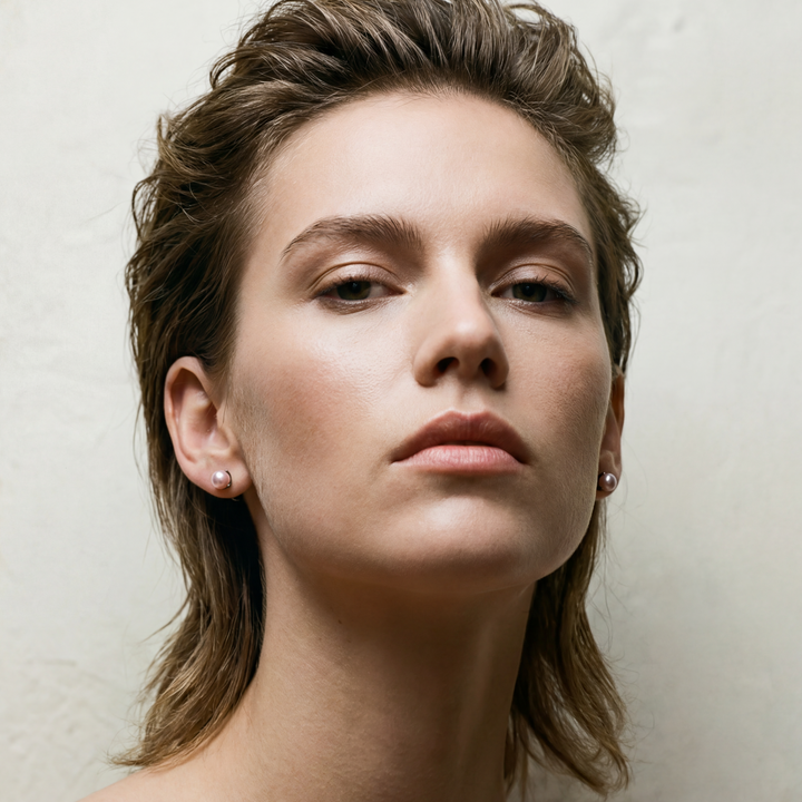 Woman with styled hair against a plain background wearing pink pearl earrings
