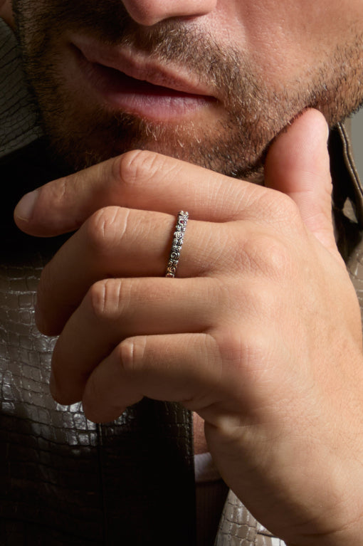 Close-up of a man's hand with a diamond ring on his finger, touching his chin.