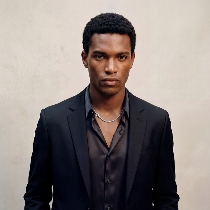 Man wearing a black suit and shirt against a beige background