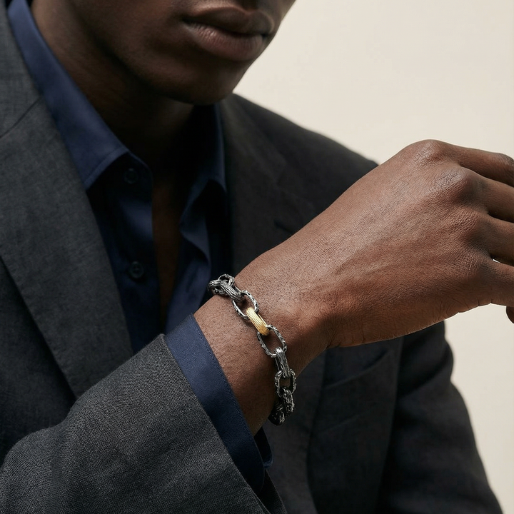 Man wearing a silver bracelet on his wrist, dressed in a gray suit and blue shirt.