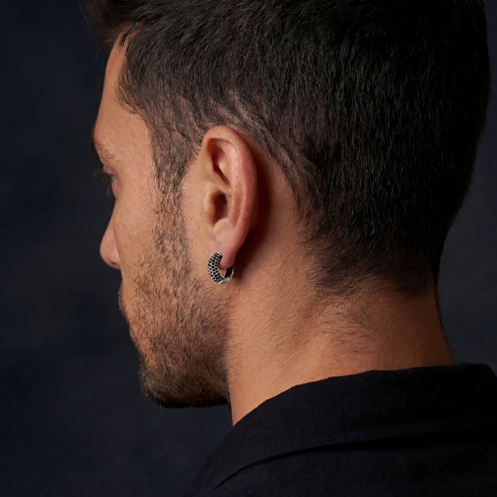 Close-up of a person wearing a black hoop earring against a dark background