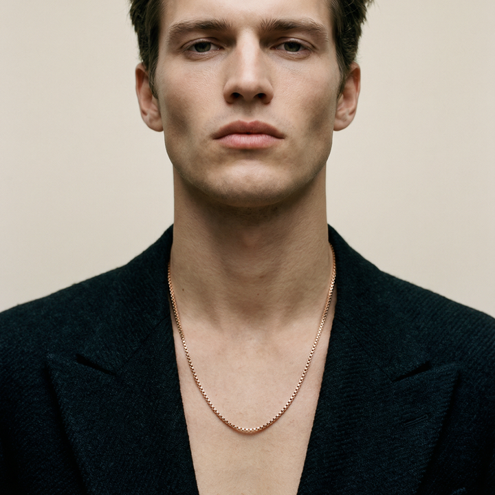 Man wearing a black blazer and gold chain necklace against a beige background