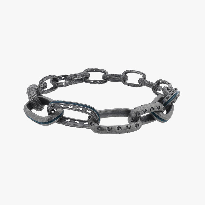 Low-angle perspective of chain bracelet displaying thick oxidized silver loops and vivid blue edge channels.