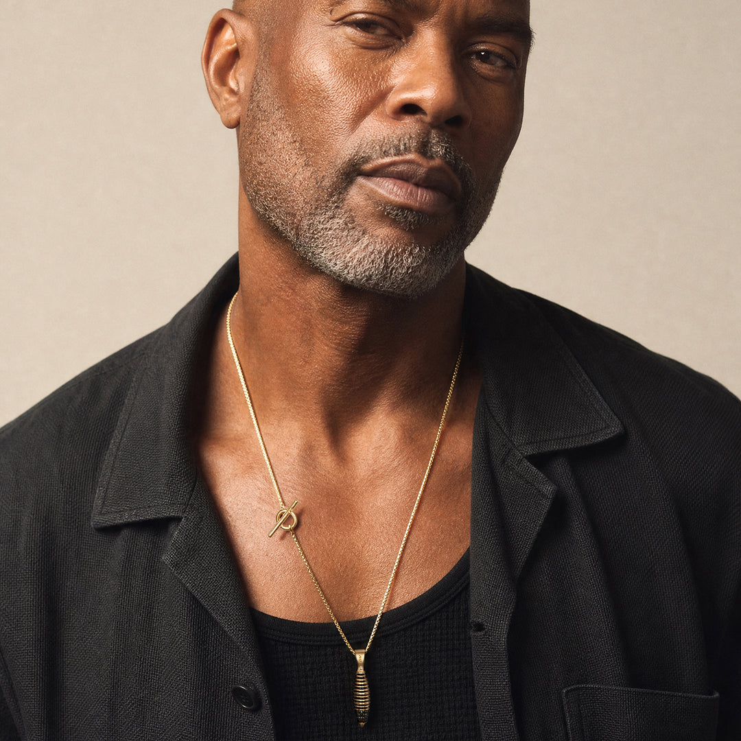 Close-up of a mature male model wearing the Acies Cocoon Gemstone Pendant in matte 18K yellow gold vermeil with black enamel detailing