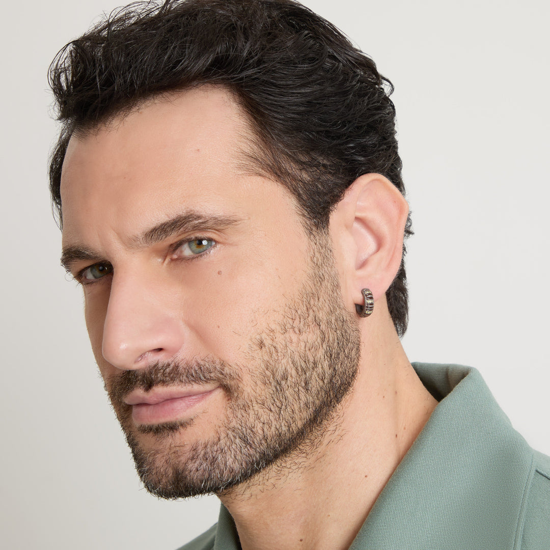 Male model wearing the MARCO DAL MASO Acies Mini Pavé Hoop Earring in oxidized silver with brown enamel and yellow sapphire accents, shown in a close-up portrait.