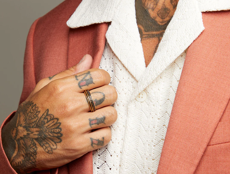 Close-up of a man wearing a gold-tone band ring with dark grooves.
