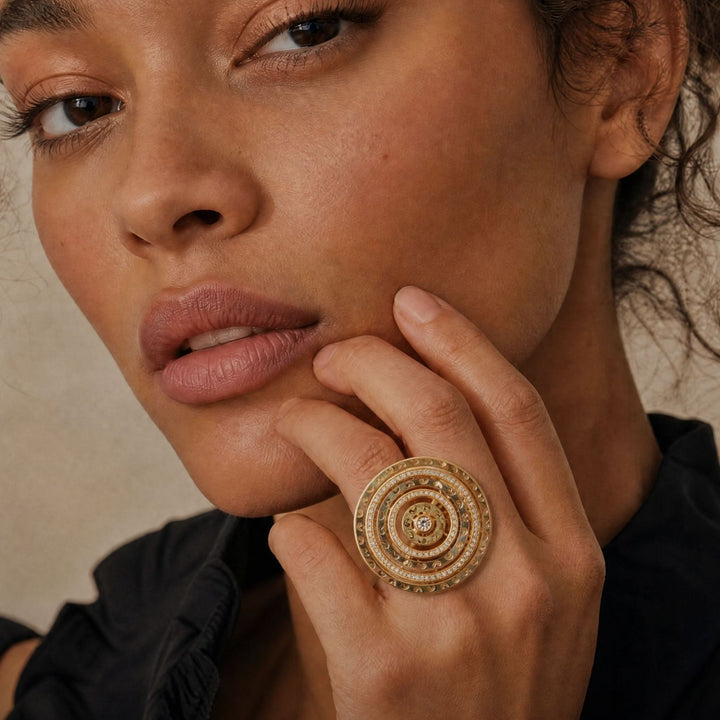 Model wearing the Amaia Twilight Ring in 18k yellow gold by MARCO DAL MASO, featuring an intricate circular design in a close-up portrait.