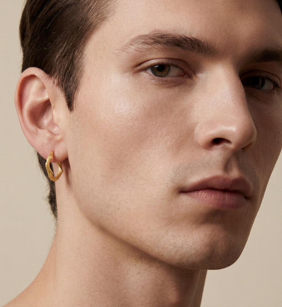 Man wearing a textured gold-tone hoop earring.