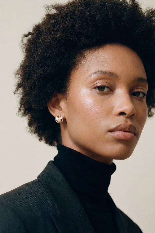 Woman wearing round gold-tone stud earrings with clear stones.