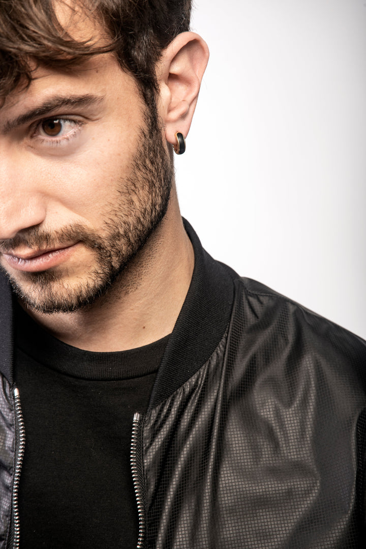 Male model wearing the MARCO DAL MASO Frame Enamel Hoop Earring in 18k yellow gold with black enamel detailing, shown in a close-up portrait styled with a black leather jacket.