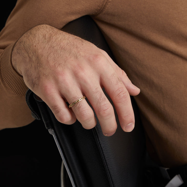Hand portrait of delicate band worn near a dark chair rest.