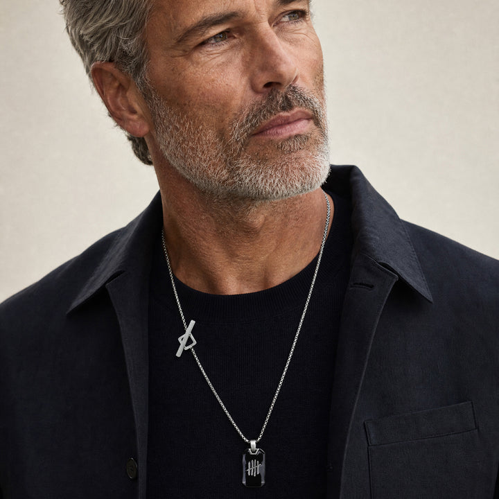 Close-up of a mature male model wearing the Triumph chain pendant in oxidised silver with black enamel detailing