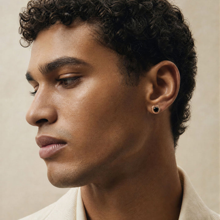 Close-up of a mixed race male model wearing the Warrior Medallion stud earring in 18K rose gold with hematite detailing