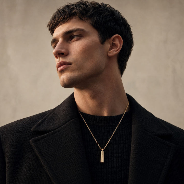 Male model wearing the ACIES Pendant in yellow gold matte vermeil and black enamel by MARCO DAL MASO, styled over a black knit sweater.