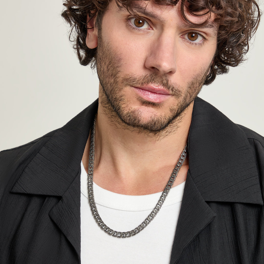 Man wearing a dark chain necklace with a repeating pattern.