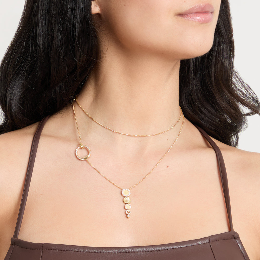 Female model wearing the MARCO DAL MASO Frammenti Cascade Pendant in 18k yellow gold, featuring cascading circular elements on a delicate gold chain, shown in a close-up neckline view.