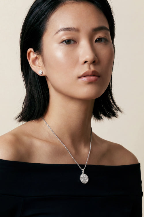 Woman wearing a silver-tone pendant necklace and matching stud earrings.
