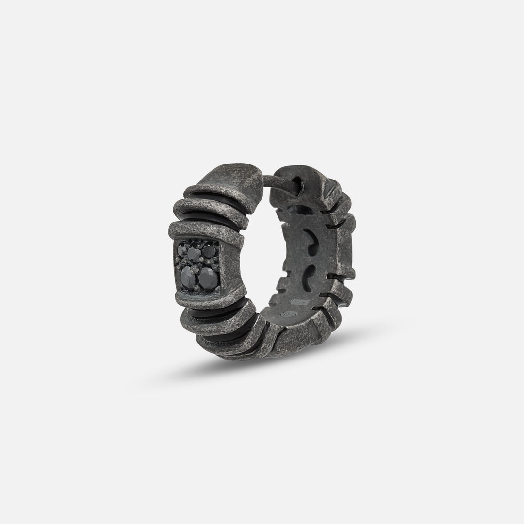 Stud ring in dark metal and black stones on a soft white stage.