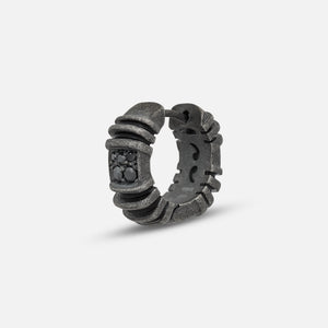 Stud ring in dark metal and black stones on a soft white stage.