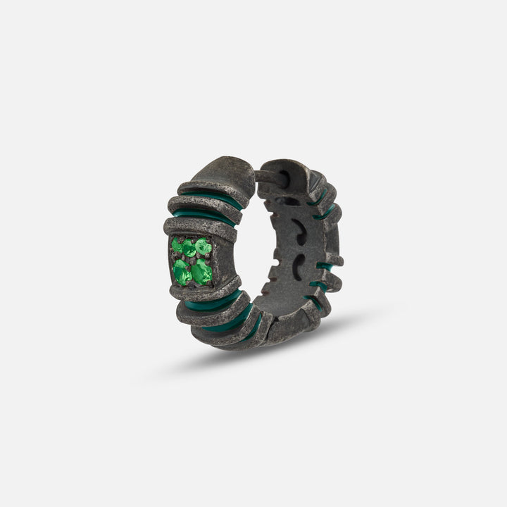 Small hoop in blackened metal and emerald stones on a bright stage.
