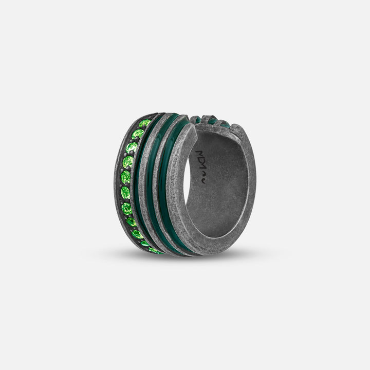 Wide band ring in distressed silver and green stones on a plain gray backdrop.
