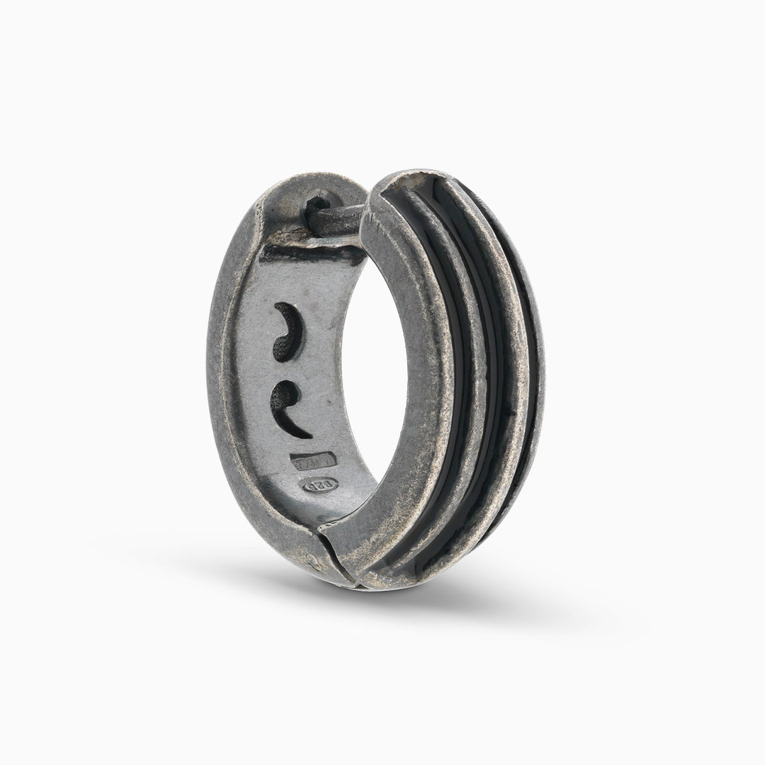 MARCO DAL MASO ACIES Huggie Earring in oxidized silver with contrasting black enamel stripes, featuring a curved hoop design and textured metal finish, shown against a light background.
