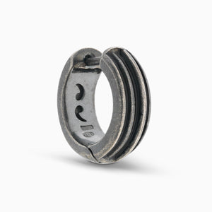 MARCO DAL MASO ACIES Huggie Earring in oxidized silver with contrasting black enamel stripes, featuring a curved hoop design and textured metal finish, shown against a light background.
