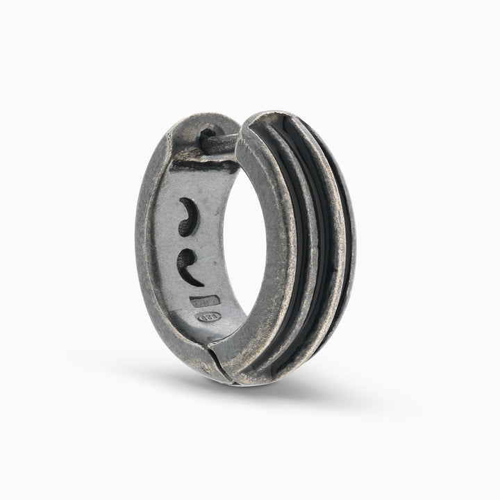 MARCO DAL MASO ACIES Huggie Earring in oxidized silver with contrasting black enamel stripes, featuring a curved hoop design and textured metal finish, shown against a light background.