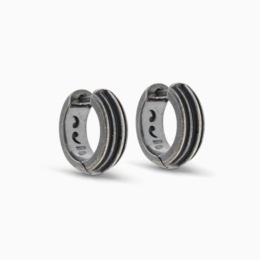Pair of MARCO DAL MASO ACIES Huggie Earrings in oxidized silver with black enamel stripes, featuring textured hoop designs, displayed against a light background.