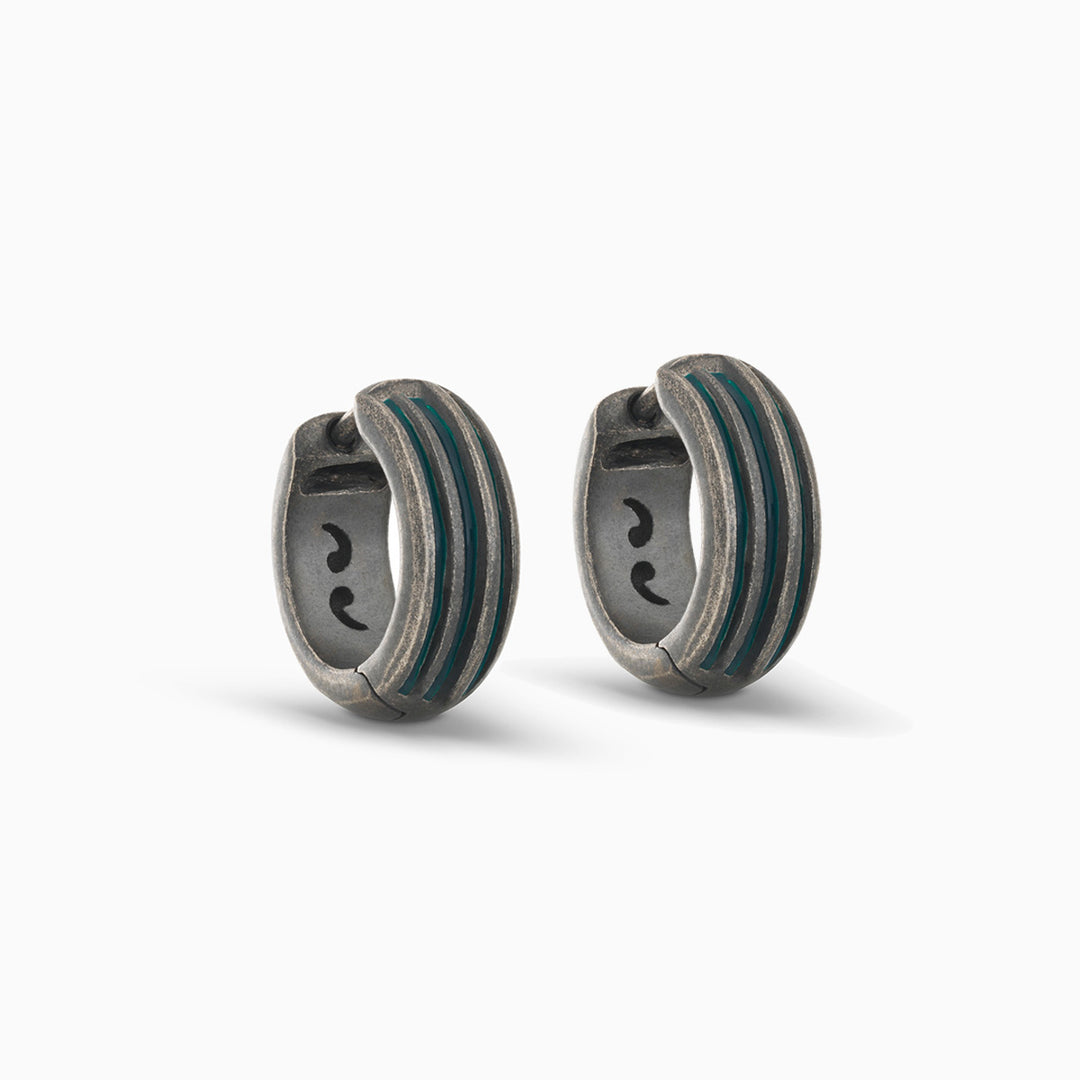 Pair of MARCO DAL MASO Acies Huggie Earrings in oxidized silver with green enamel stripes, featuring a curved hoop design and textured metal finish, displayed against a light background.