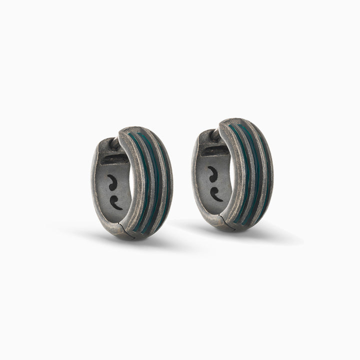 Pair of MARCO DAL MASO Acies Huggie Earrings in oxidized silver with green enamel stripes, featuring a curved hoop design and textured metal finish, displayed against a light background.