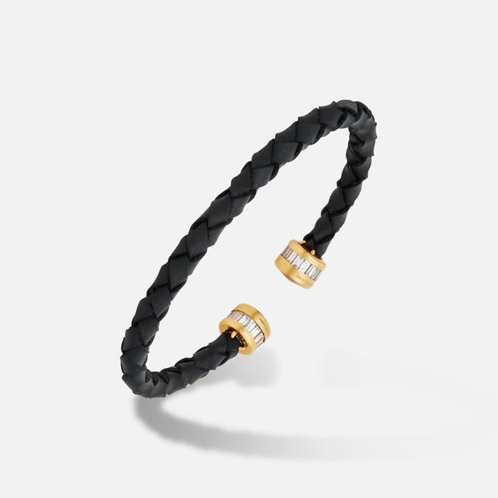 Cuff bracelet in black leather and yellow gold with white gems on an ivory floor.