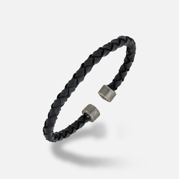 MARCO DAL MASO Acies Leather Cuff featuring braided black leather, oxidized silver end caps, and black enamel detailing, shown in an angled product view against a light background.