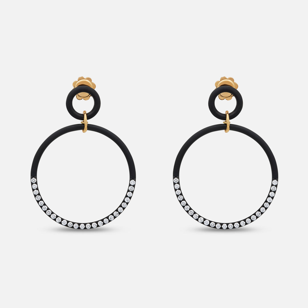 MARCO DAL MASO Eclipse Twin Orbit Earrings in black titanium, featuring double circular hoops with sparkling stone-set detailing and gold-tone connectors, displayed against a light background.
