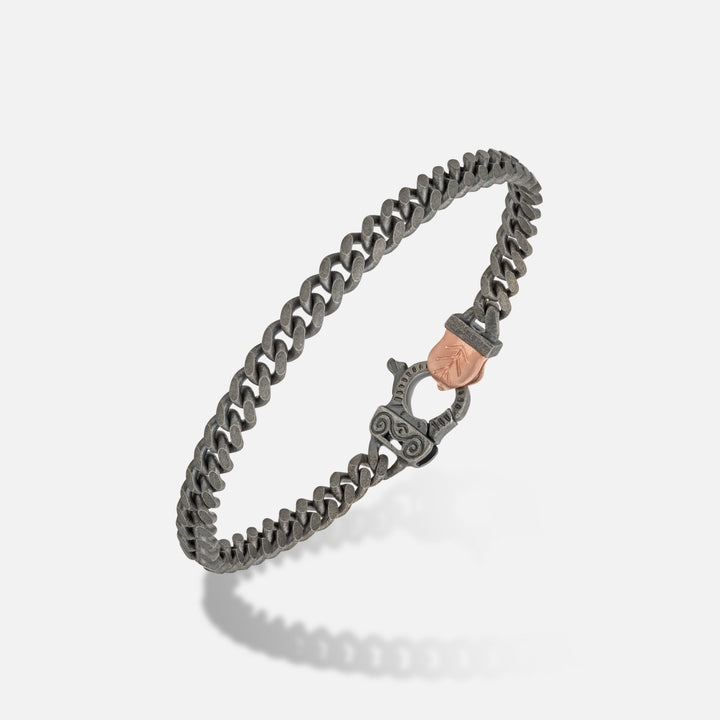 Curved link in dark steel and rose accent on a shadow stage.