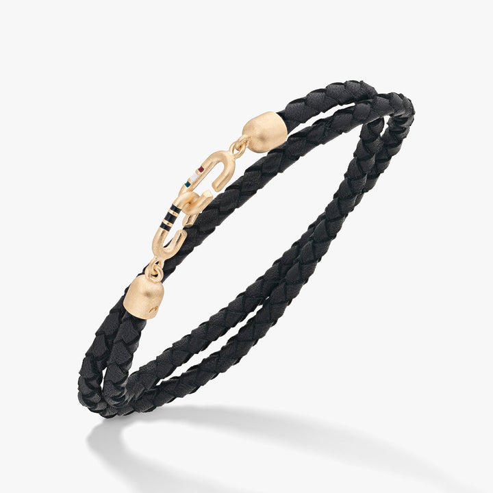 Wrap bracelet in black leather and gold tone on a soft white stage.
