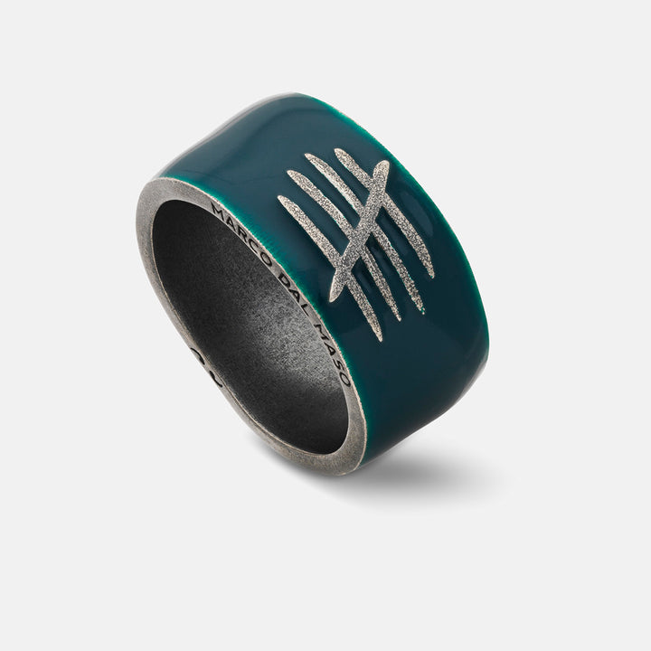 Angled shot of wide ring showing teal enamel with silver crest on neutral surface.
