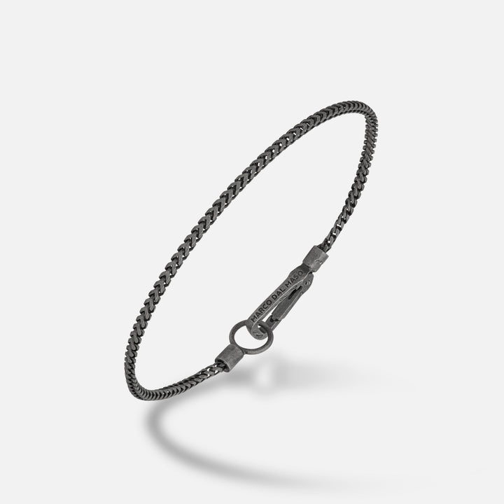 Sleek chain in dark metal and blackened steel on a pale gradient stage.