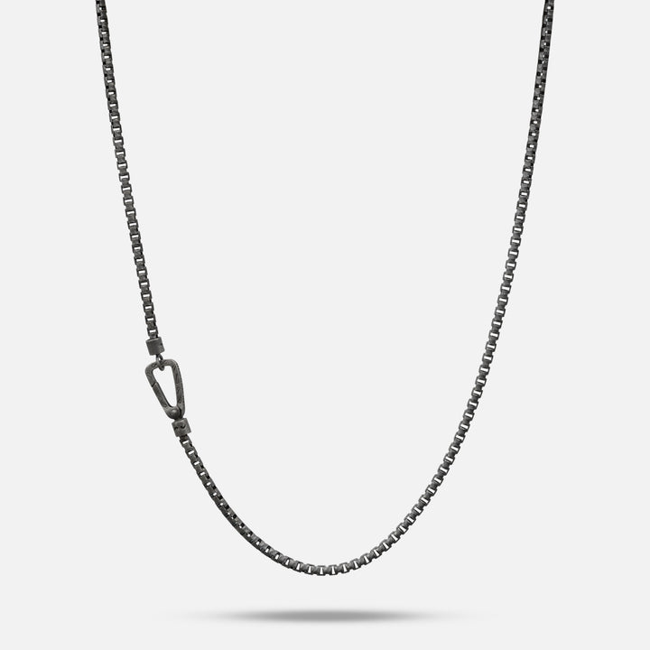 Box chain in gunmetal tone and clasp hardware on a soft plane.