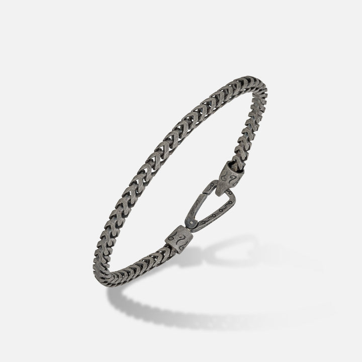Woven chain in aged sterling silver on an angled studio floor.